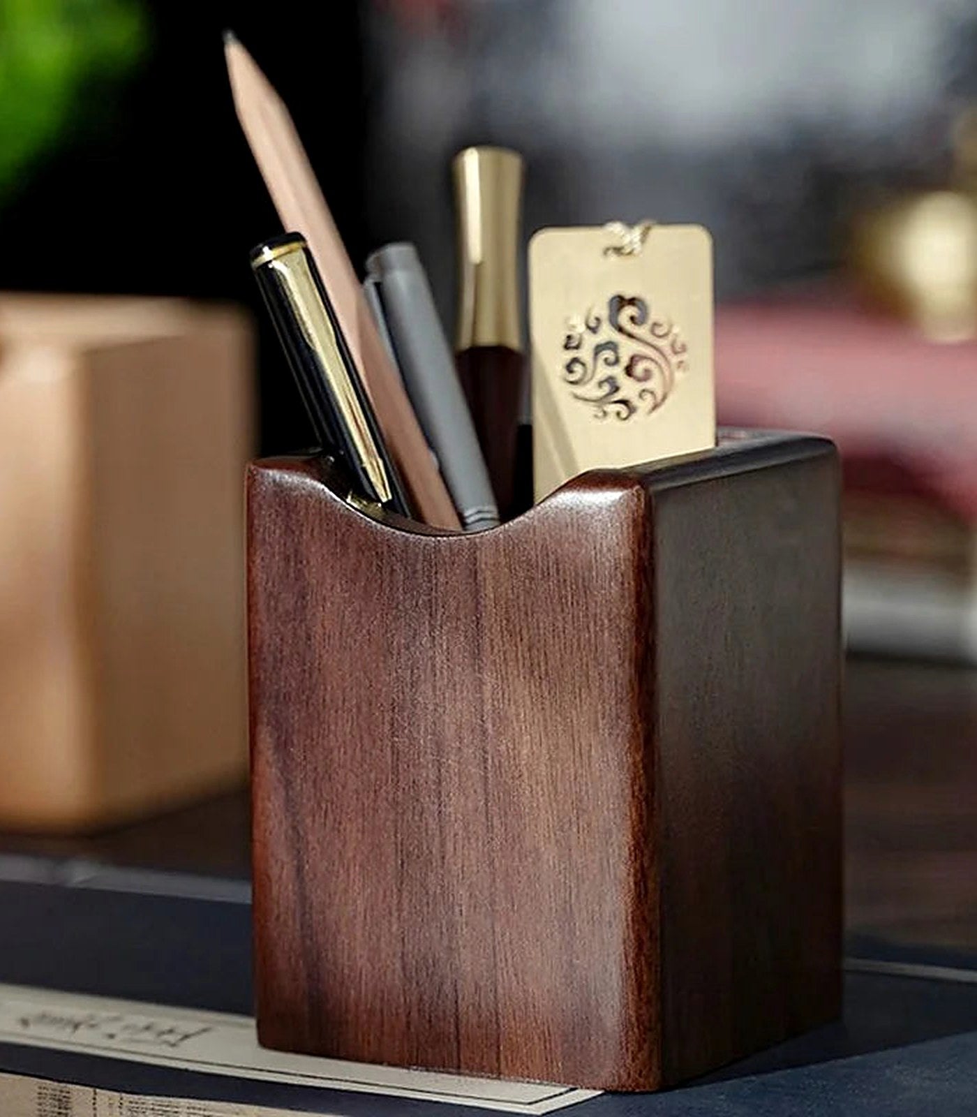A walnut pen holder on a desk holding pens and a pencil