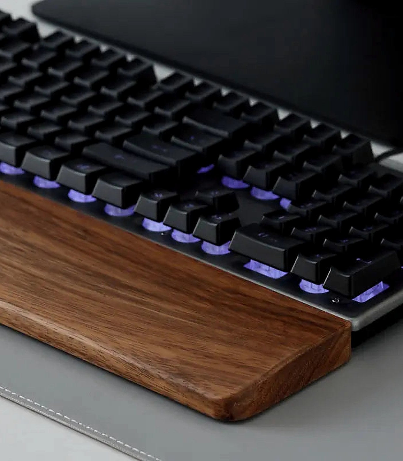 A mechanical keyboard resting against a solid walnut wrist rest