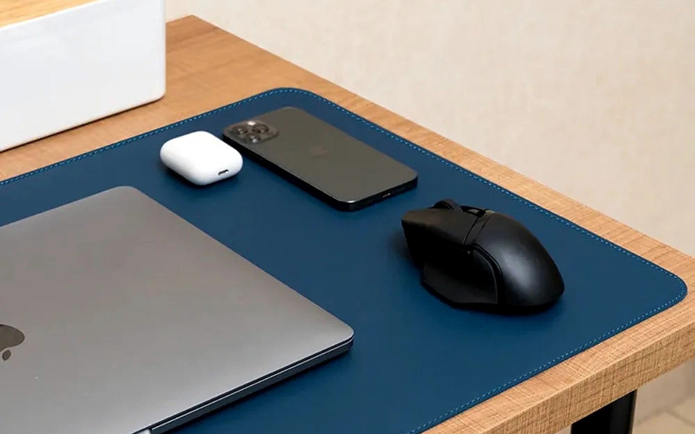 A wood desk with a navy leather desk pad, laptop, phone and mouse
